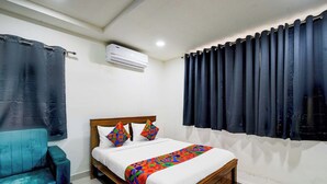 A bedroom with a bed, a chair, a window with curtains, and an air conditioning unit. - Fabhotel Aashvi (Hyderabad)