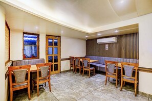 Un espace repas avec des tables et des chaises en bois, un banc et une vue sur l’extérieur par une fenêtre.