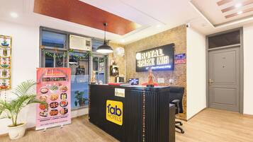 A hotel reception area with a sign for Royal Spark Inn, a reception desk, a clock, and a plant.
