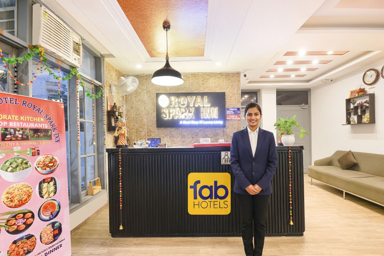 Zona de recepción de hotel con un cartel de Royal Spark Inn, un interior moderno que incluye un mostrador de recepción, un sofá y un reloj en la pared.