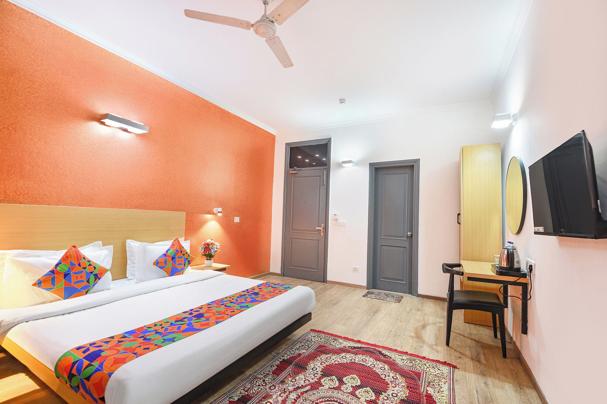 A hotel room with a bed, a desk, a chair, a television, and a ceiling fan.