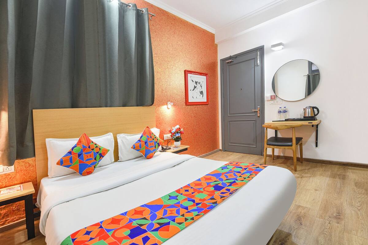 Habitación de hotel con cama, escritorio, silla, espejo y puerta.