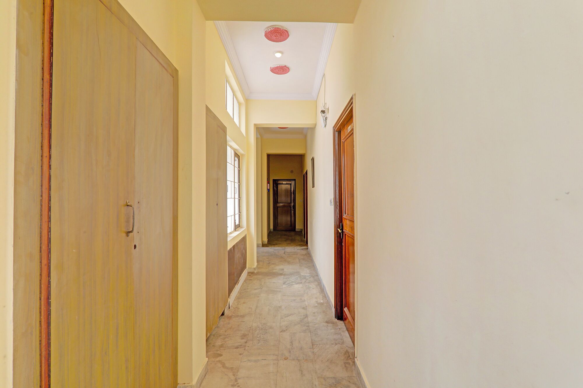A narrow hallway with wooden doors on both sides, a tiled floor, and a ceiling with recessed lighting.