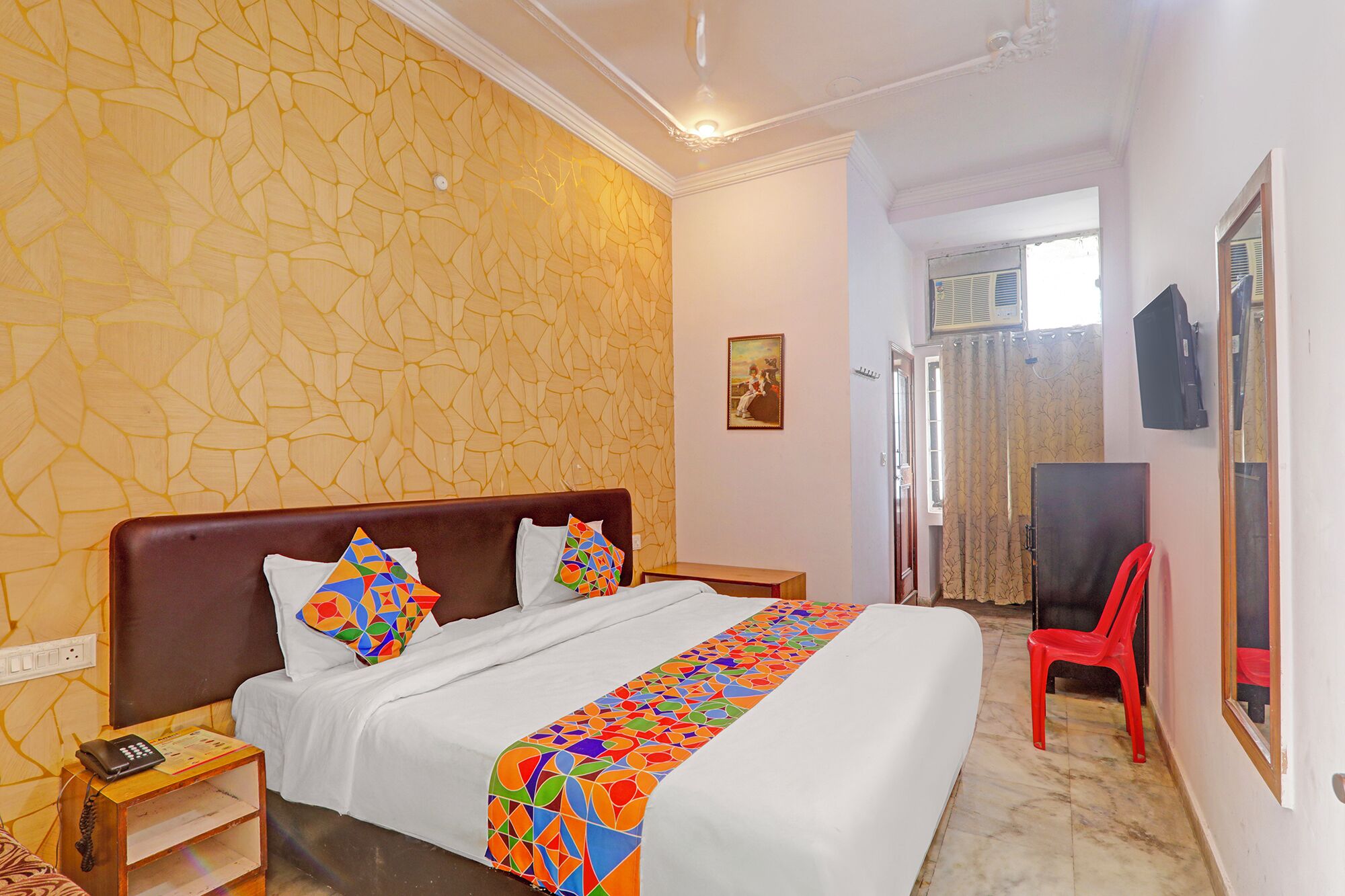 A hotel room with a bed, a nightstand, a red chair, and a painting on the wall.