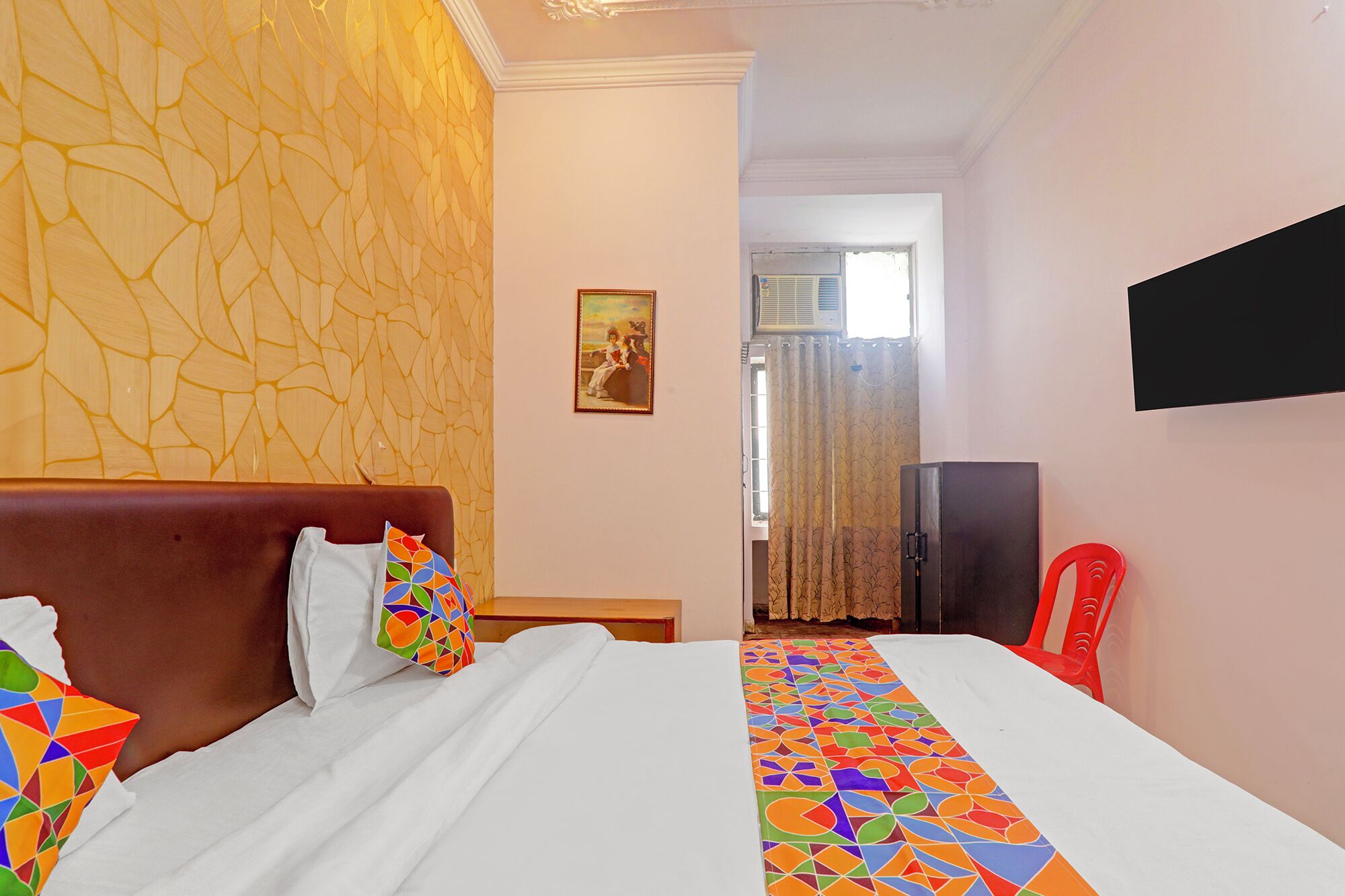 Una habitación de hotel con cama, televisión y ventana con cortinas.