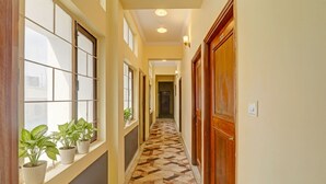 A hallway with a patterned floor, large windows with potted plants, and wooden doors. - Fabhotel Anant (Lucknow)