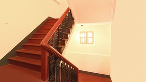 Una escalera con escalones de madera y barandillas de metal, que conduce a un rellano con un pequeño ventanal.