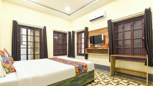 Una habitación de hotel con cama, televisión y ventana con cortinas.