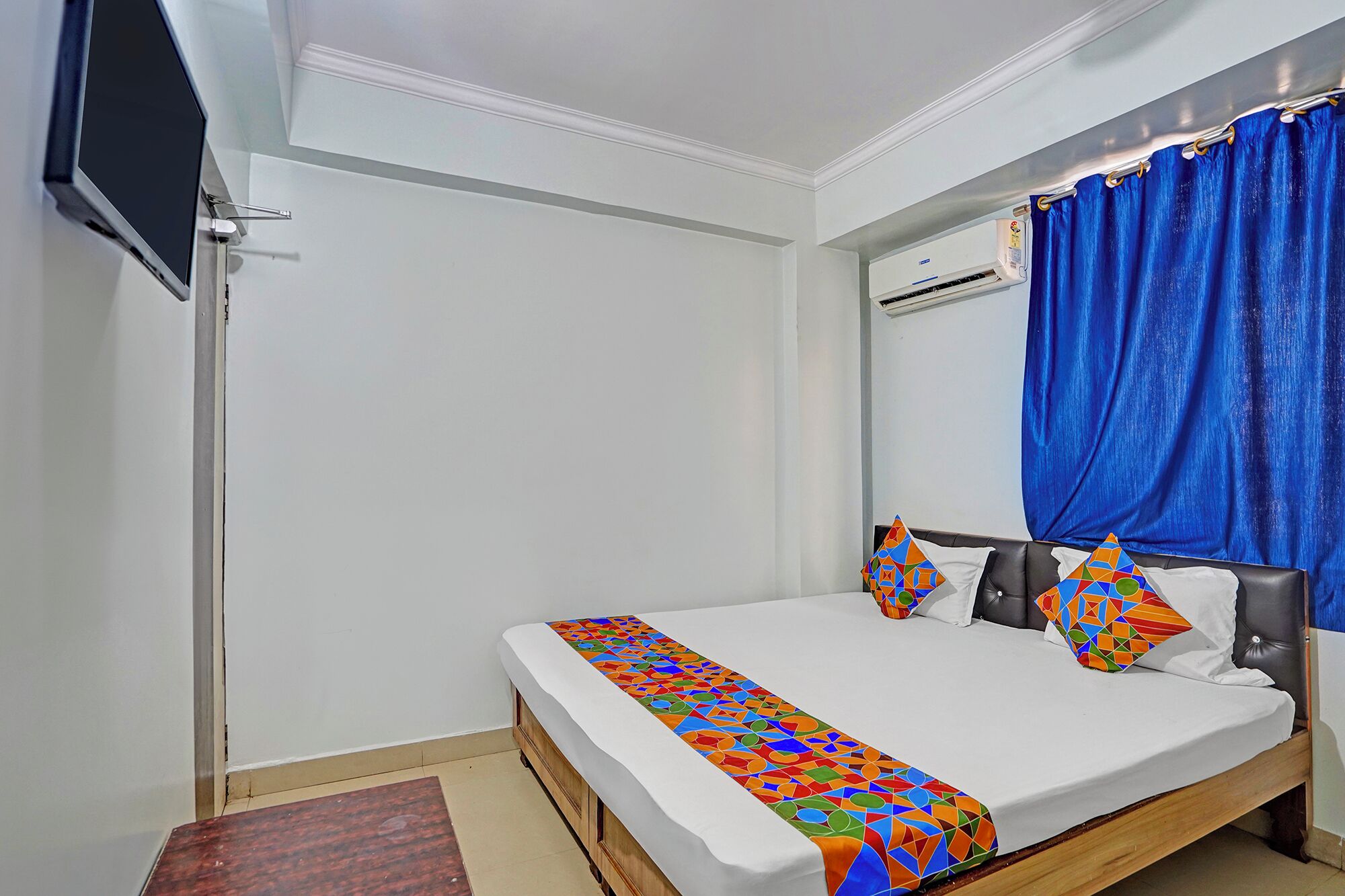 Un dormitorio con cama, televisión, aire acondicionado y ventana con cortinas azules.