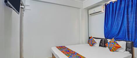 Un dormitorio con cama, televisión, aire acondicionado y ventana con cortinas azules.