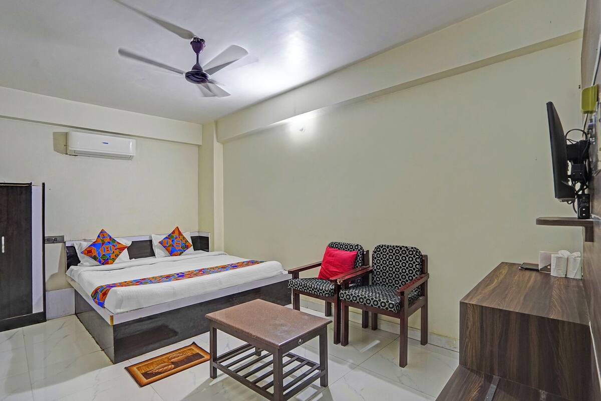 A hotel room with a bed, two patterned chairs, a small table, a television, and a ceiling fan.