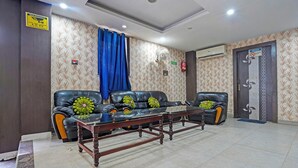 A lobby with leather sofas, a wooden coffee table, patterned wallpaper, a blue curtain, and a door with a no-smoking sign.