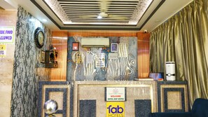 A hotel reception area with a marble wall, a clock, a mirror, a cash register, and a sign indicating CCTV surveillance. - FabHotel Reconnect Suites - Near IGI Airport - New Delhi (New Delhi)