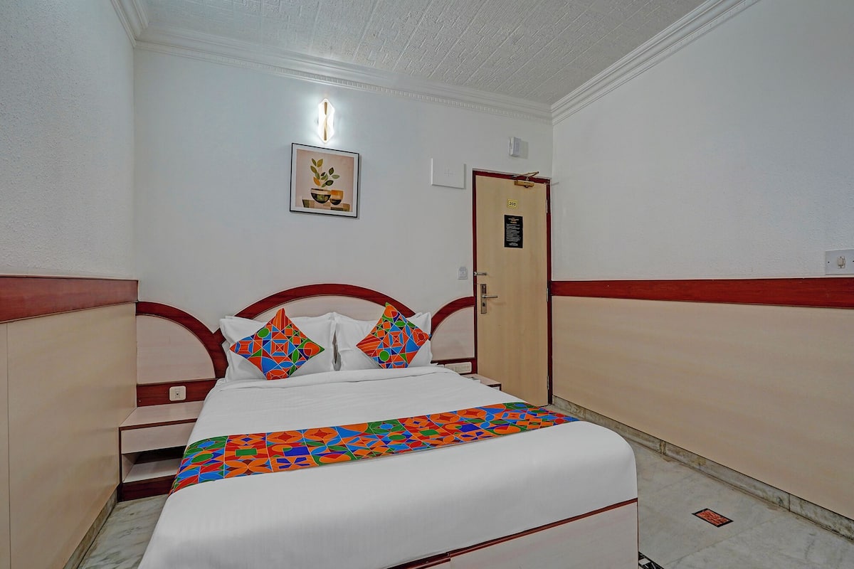 A hotel room with a bed, a wooden headboard, a door, and a framed picture on the wall.