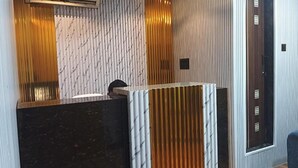 A reception area with a dark reception desk, a white textured wall, and a wooden panel. - Fabhotel Arya Baner (Pune)