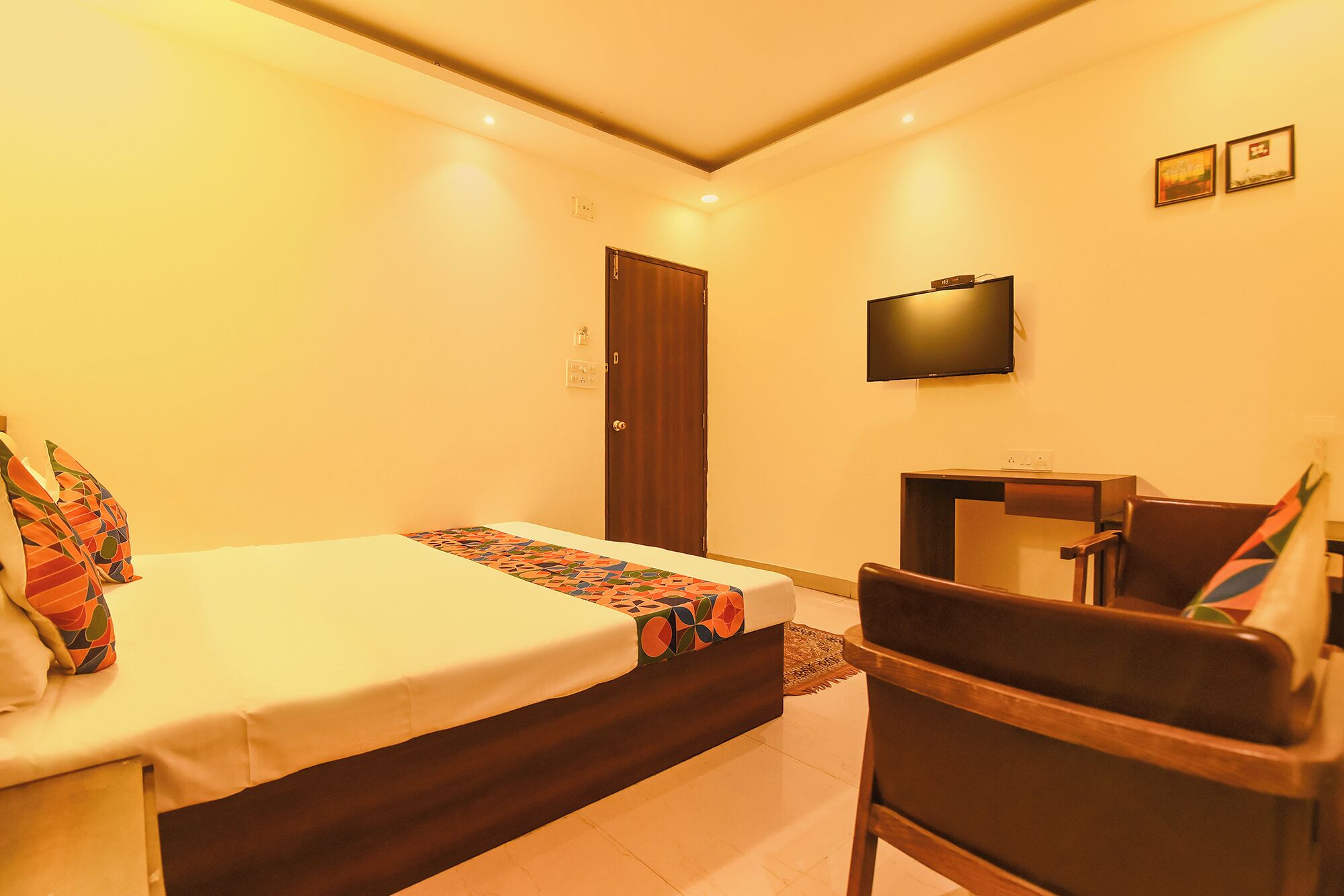 A hotel room with a bed, a desk, a chair, a television, and a door.