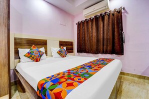A neatly made bed with white linens and colorful geometric pillows, a wooden headboard, and a brown curtain.