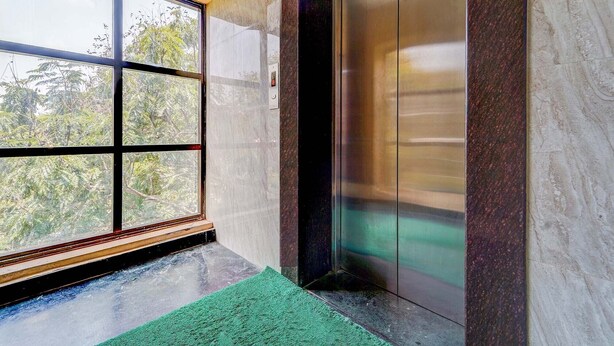 An elevator with a glass door, a green mat at the entrance, and a view of trees outside. - Fabhotel Sahana Residency (Chennai)