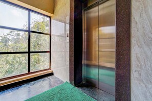 An elevator with a glass door, a green mat at the entrance, and a view of trees outside. - Fabhotel Sahana Residency (Chennai)