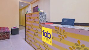 Zona de recepción con el letrero de 'Tab Hotels', un mostrador de recepción, una silla azul y una pequeña mesa con una caja de pañuelos.