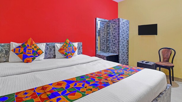 Una cama con una colcha de diseño geométrico y colores vivos, una pared roja, un espejo y una silla.