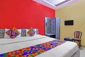 A bed with a colorful geometric-patterned bedspread, a red wall, a mirror, and a chair. - Fabhotel Swagatam (Barasat)