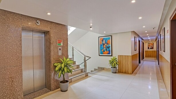 A modern hotel lobby with a marble elevator, a staircase, and potted plants. - FabHotel The Tuesday Suits - Opposite to Delhi Public School (Noida)