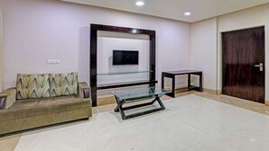 A living room with a sofa, a glass coffee table, a TV mounted on a wall, and a wooden door. - FabHotel The Tuesday Suits - Opposite to Delhi Public School (Noida)