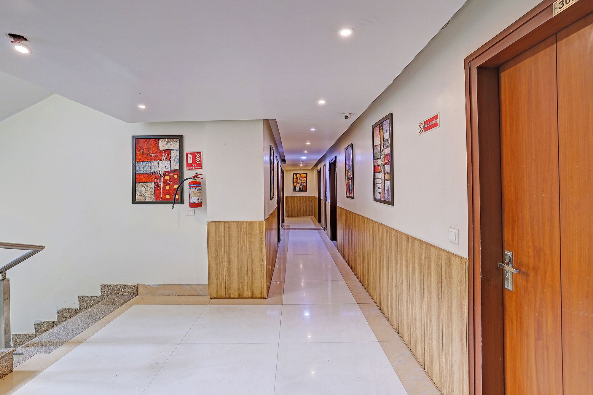Pasillo de hotel con paneles de madera, un extintor y un cartel de 'No Fumar'.
