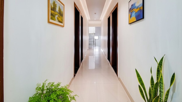 A hallway with a tiled floor, framed artwork on the walls, and a potted plant. - FabExpress Abhishek (Pune)