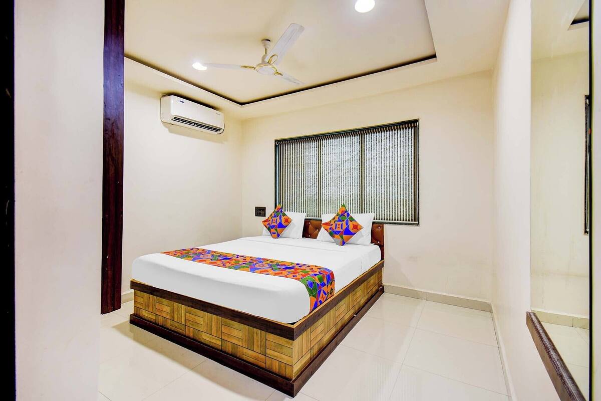A bedroom with a bed, a ceiling fan, an air conditioning unit, and a window with blinds.