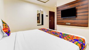 A hotel room with a bed, a TV mounted on a wooden panel, a door, and a mirror on the wall. - FabExpress Abhishek (Pune)