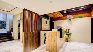 A hotel reception area with a wooden reception desk, a digital screen, and an exit sign. - Fabhotel Alfa (Vijayawada)
