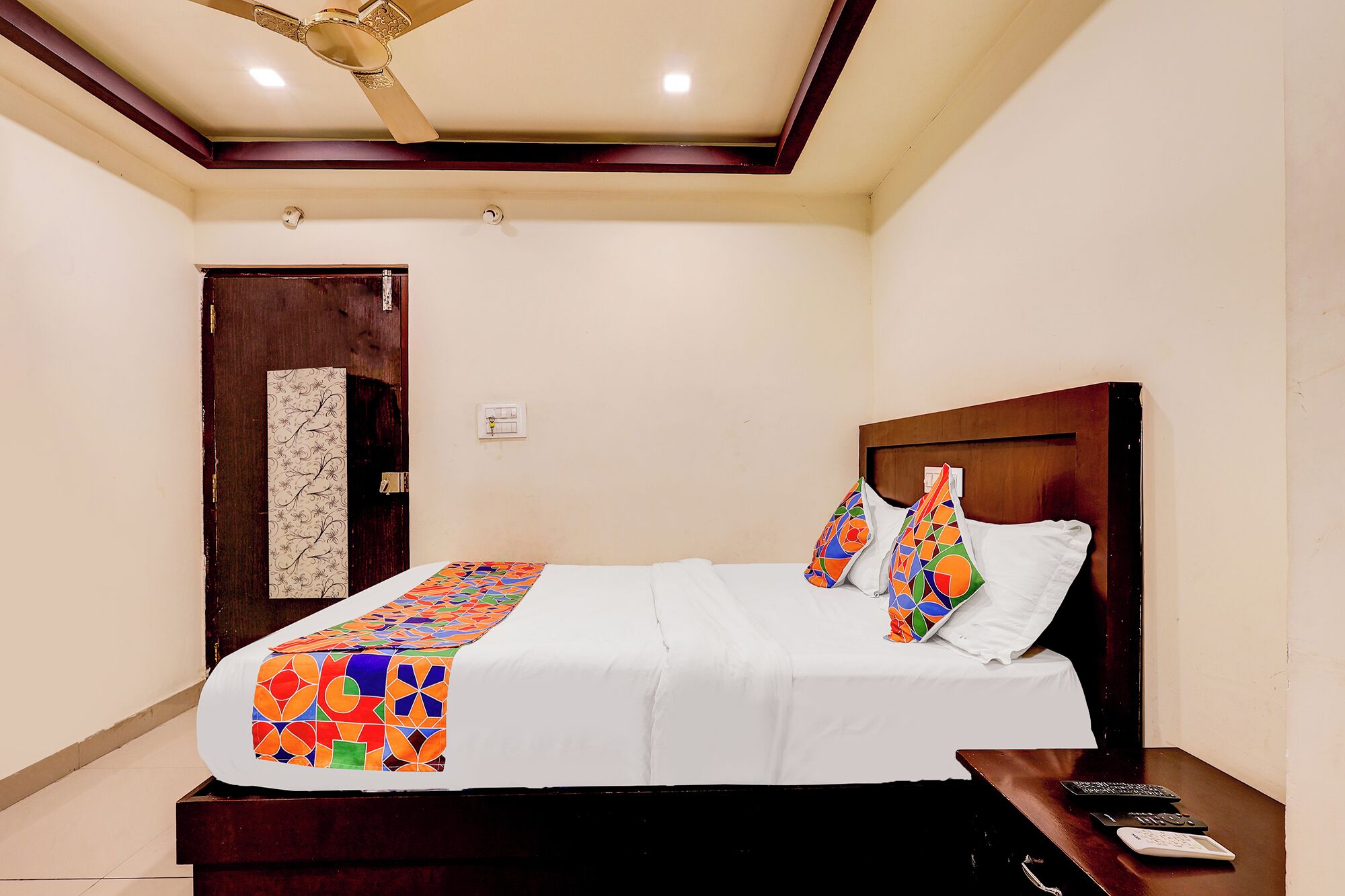 A hotel room with a bed, a wooden headboard, a nightstand, a desk, and a ceiling fan.