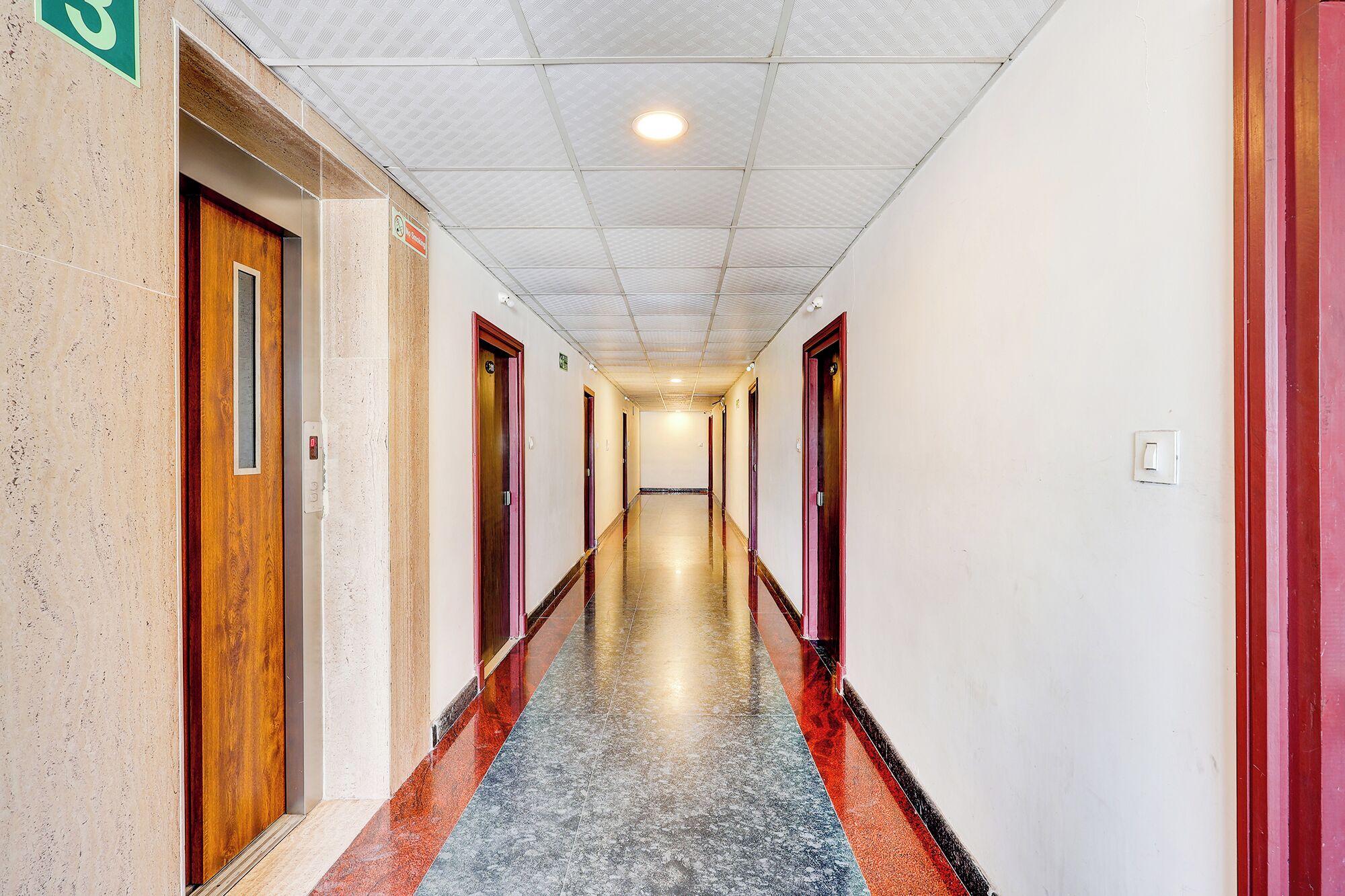 Un couloir d’hôtel avec de nombreuses portes, un sol carrelé et un plafond orné d’un motif en réseau.