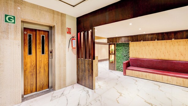 A hotel lobby with a marble floor, a wooden elevator, a red bench, and a green wall. - Fabhotel Alfa (Vijayawada)