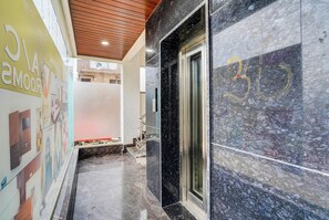 Um corredor com piso de mármore, teto de madeira e porta de elevador de vidro.