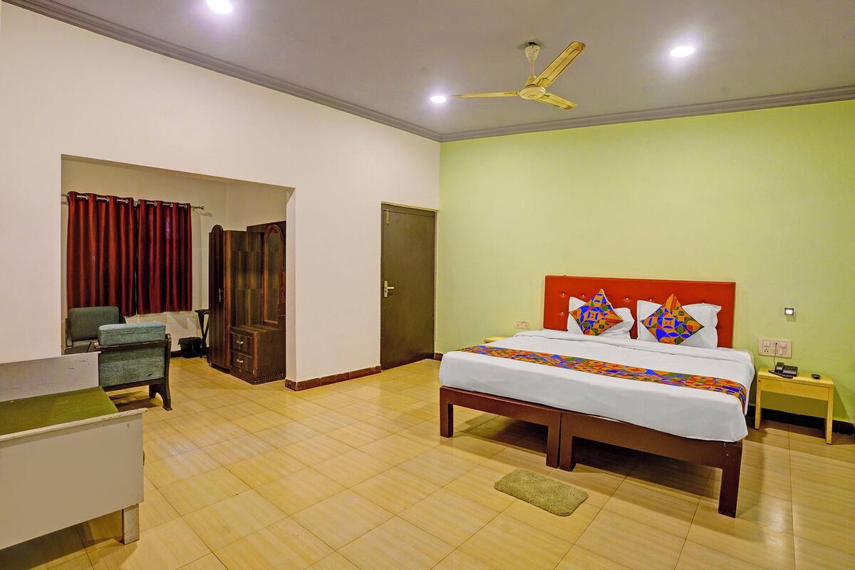 A hotel room with a bed, bedside table, nightstand, and a desk with a chair.