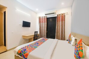 A hotel room with a bed, a desk, a chair, a television, and an air conditioning unit. - Fabhotel X Green Tree (Gurugram)