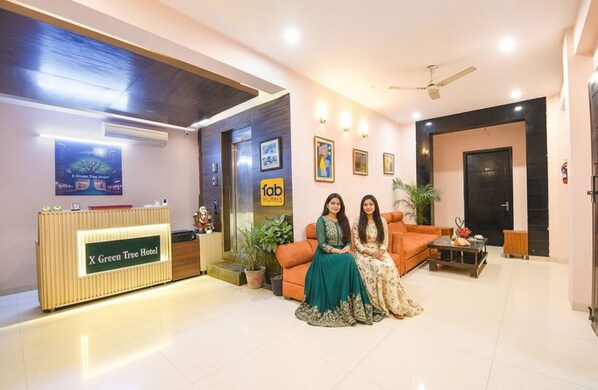 A reception area with a reception desk labeled "X Green Tree Hotel," a sofa, a coffee table, and a ceiling fan.