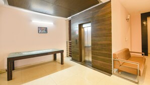 A lobby with a bench, a sofa, an elevator, and a wall-mounted picture. - Fabhotel X Green Tree (Gurugram)