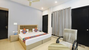 A bedroom with a bed, bedside table, chair, and a ceiling fan. - Fabhotel X Green Tree (Gurugram)