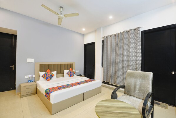 A bedroom with a bed, bedside table, chair, and a ceiling fan. - Fabhotel X Green Tree (Gurugram)