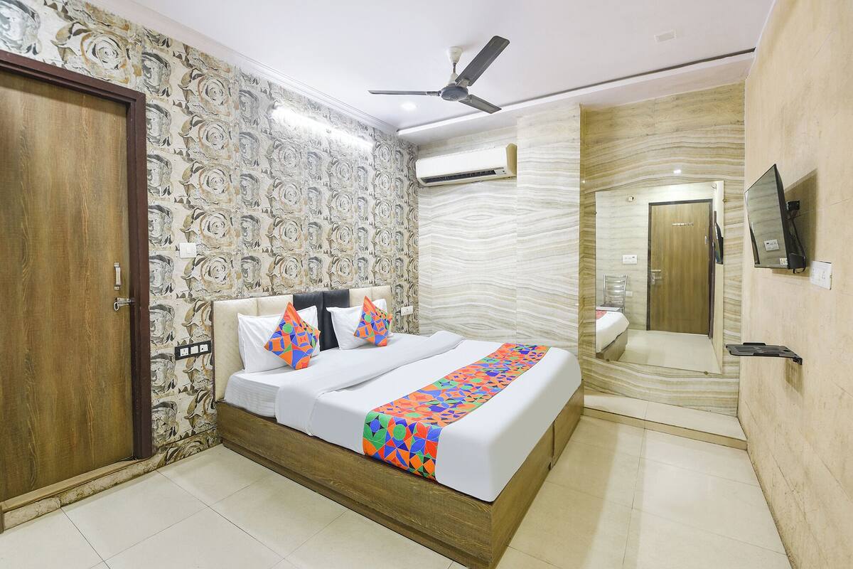 A bedroom with a bed, a ceiling fan, an air conditioning unit, a mirror, and a wooden door.