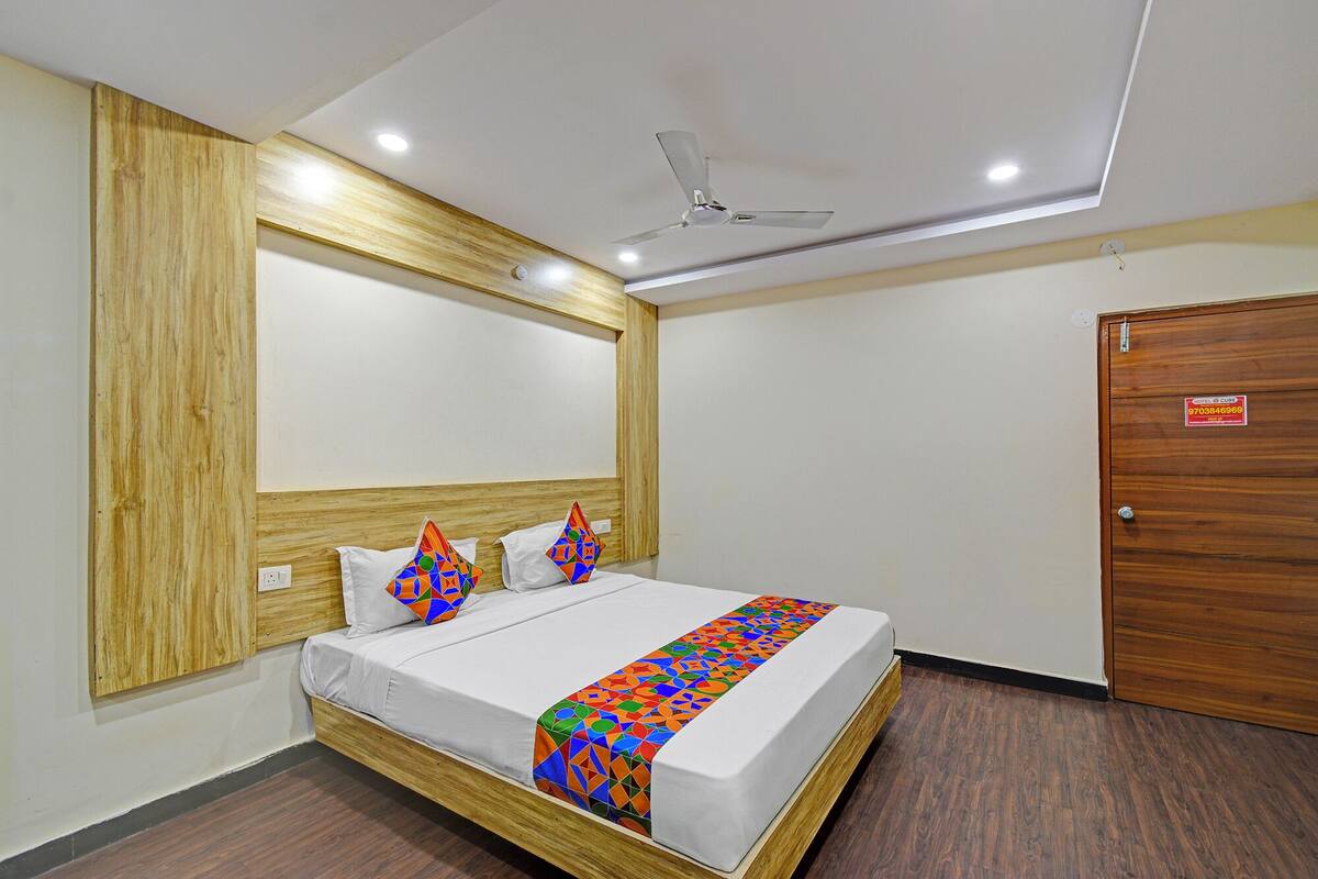 Ein Hotelzimmer mit hölzernem Kopfteil, einem Bett mit farbenfroher geometrischer Bettwäsche, einem Deckenventilator und einer Holztür.