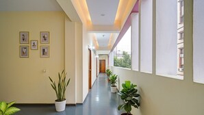 A corridor with potted plants, framed pictures on the wall, and large windows. - Fabhotel Cube (Hyderabad)