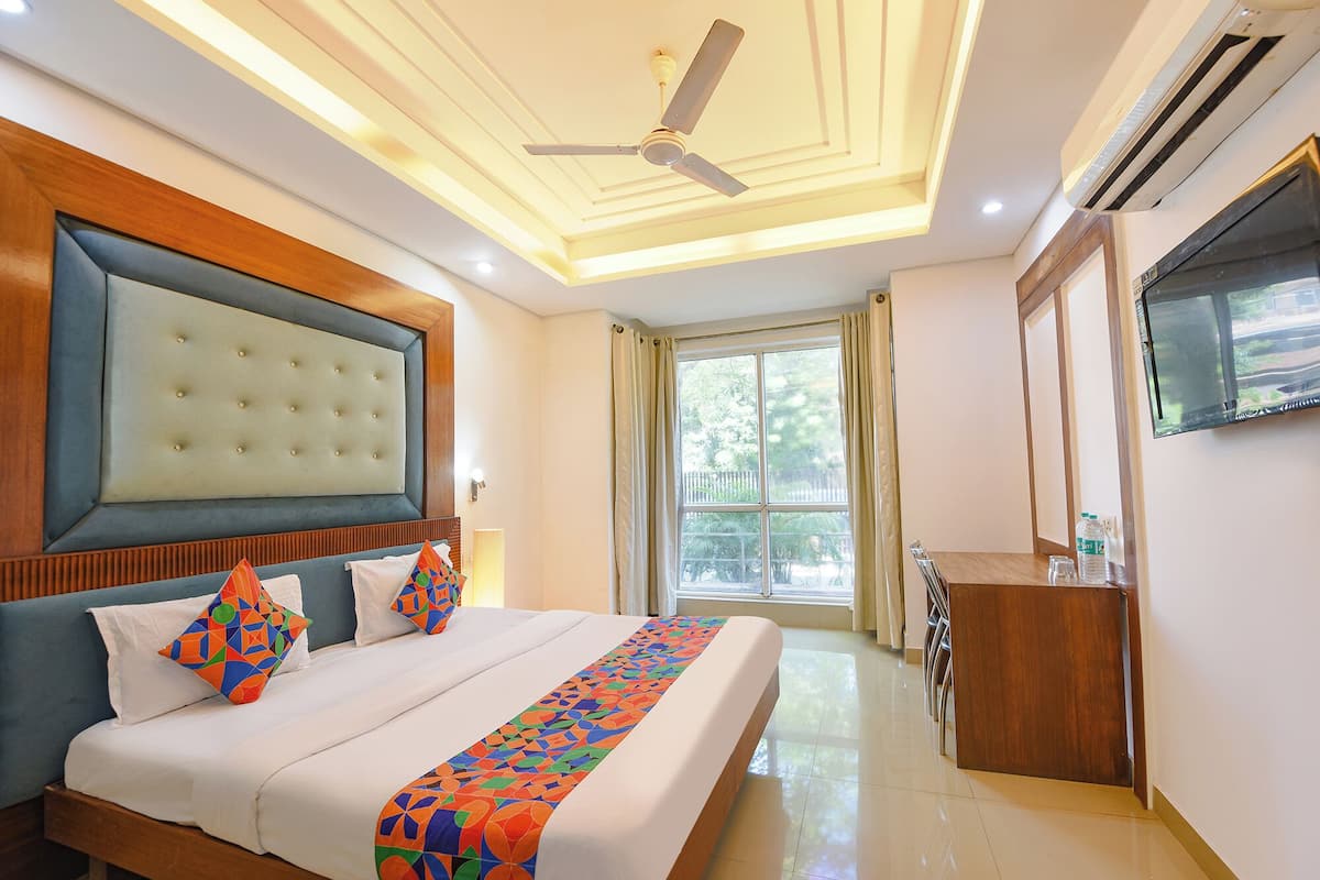A hotel room with a large bed, a ceiling fan, a TV, and a window with curtains.