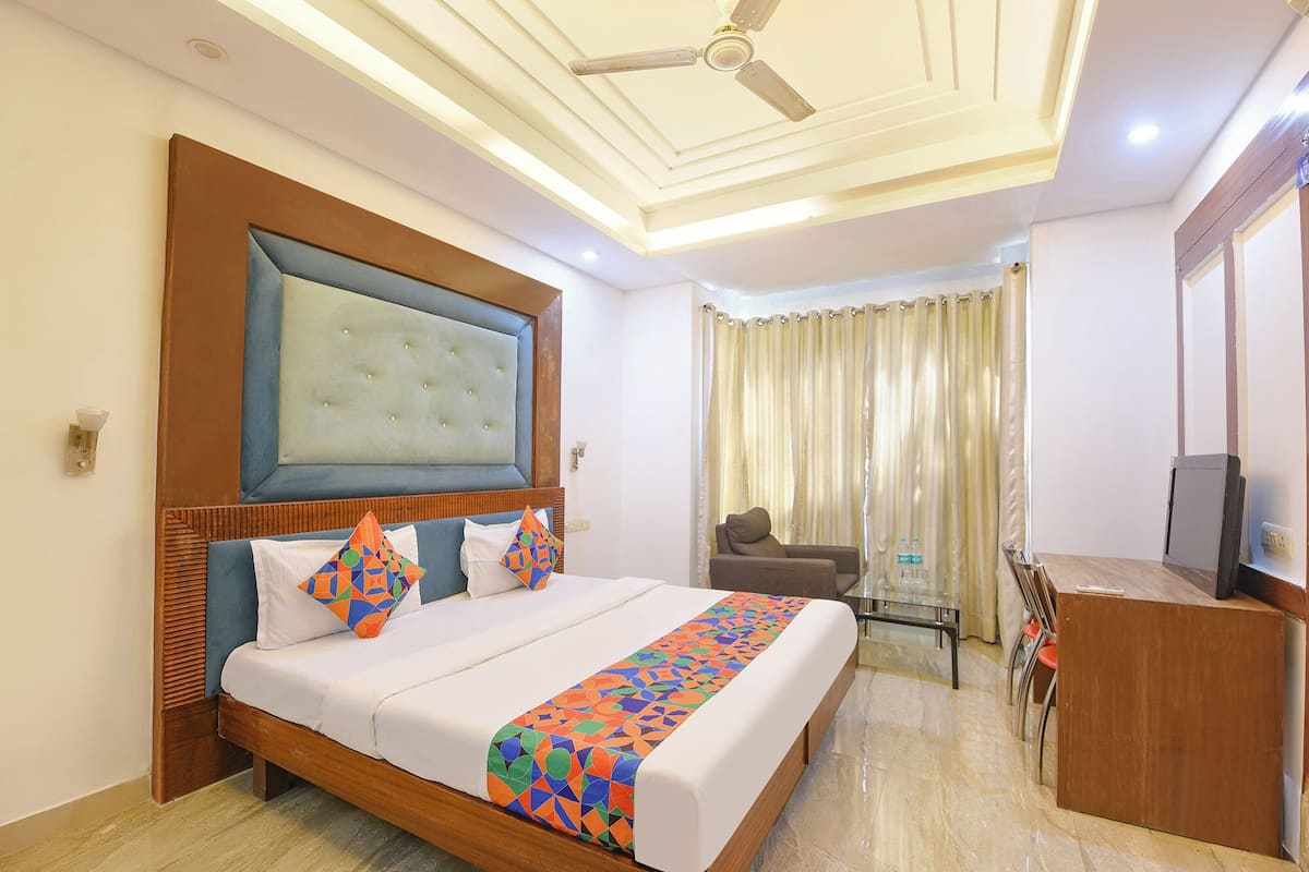 A hotel room with a large bed, a desk, a chair, a television, and a ceiling fan.