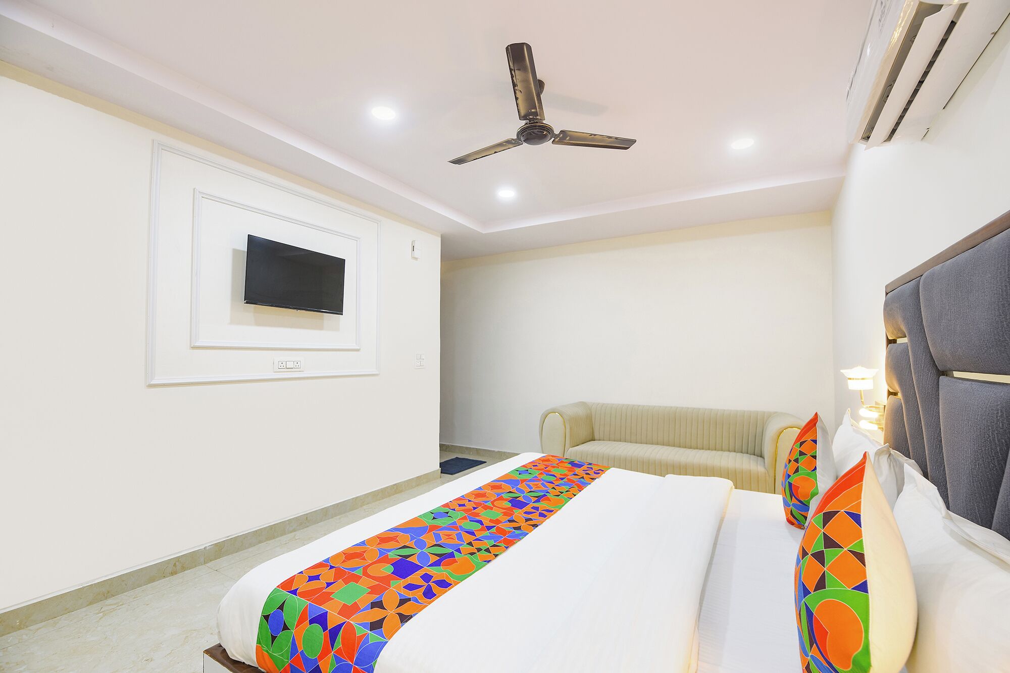 Une chambre d’hôtel avec un lit, un canapé, un ventilateur de plafond, un téléviseur fixé au mur et une fenêtre.