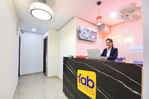 Ein Empfangsbereich mit einem 'fab hotels'-Logo, einem Fernseher, einer Neonreklame und einem Ventilator.